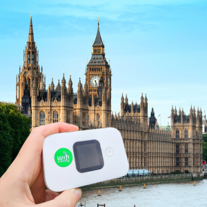 Hand presenting a portable WiFi gadget in front of British house of parliament in London.