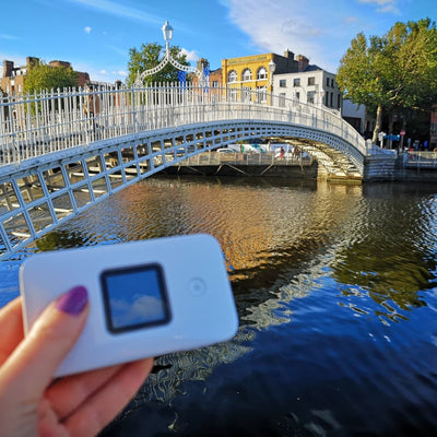 Portable WiFi device in the grasp of a person with the Ha'penny bridge, Dublin, in the background.